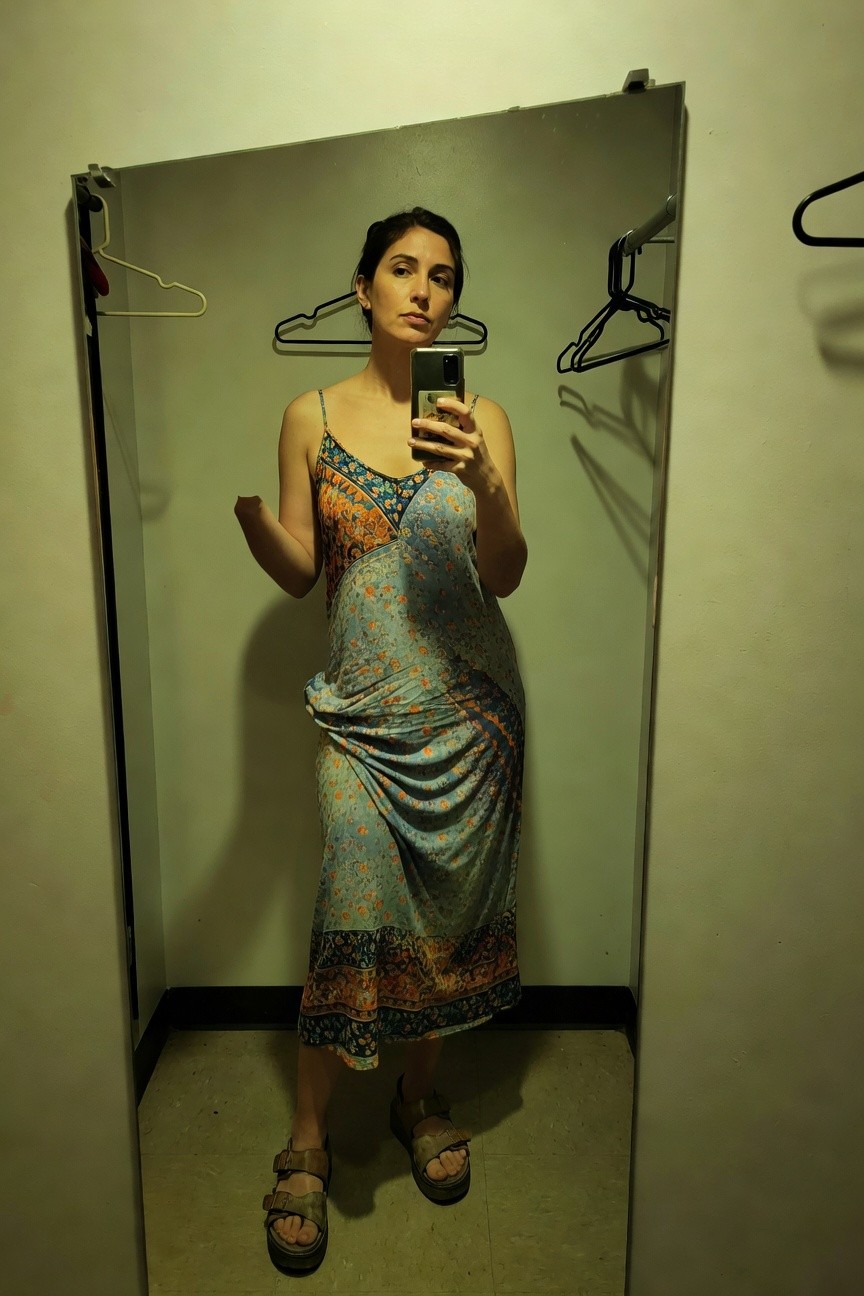 Woman taking a mirror selfie in a fitting room while wearing a flowy boho maxi dress with colorful turquoise, orange, and floral prints, spaghetti straps, side drape, and chunky tan leather sandals