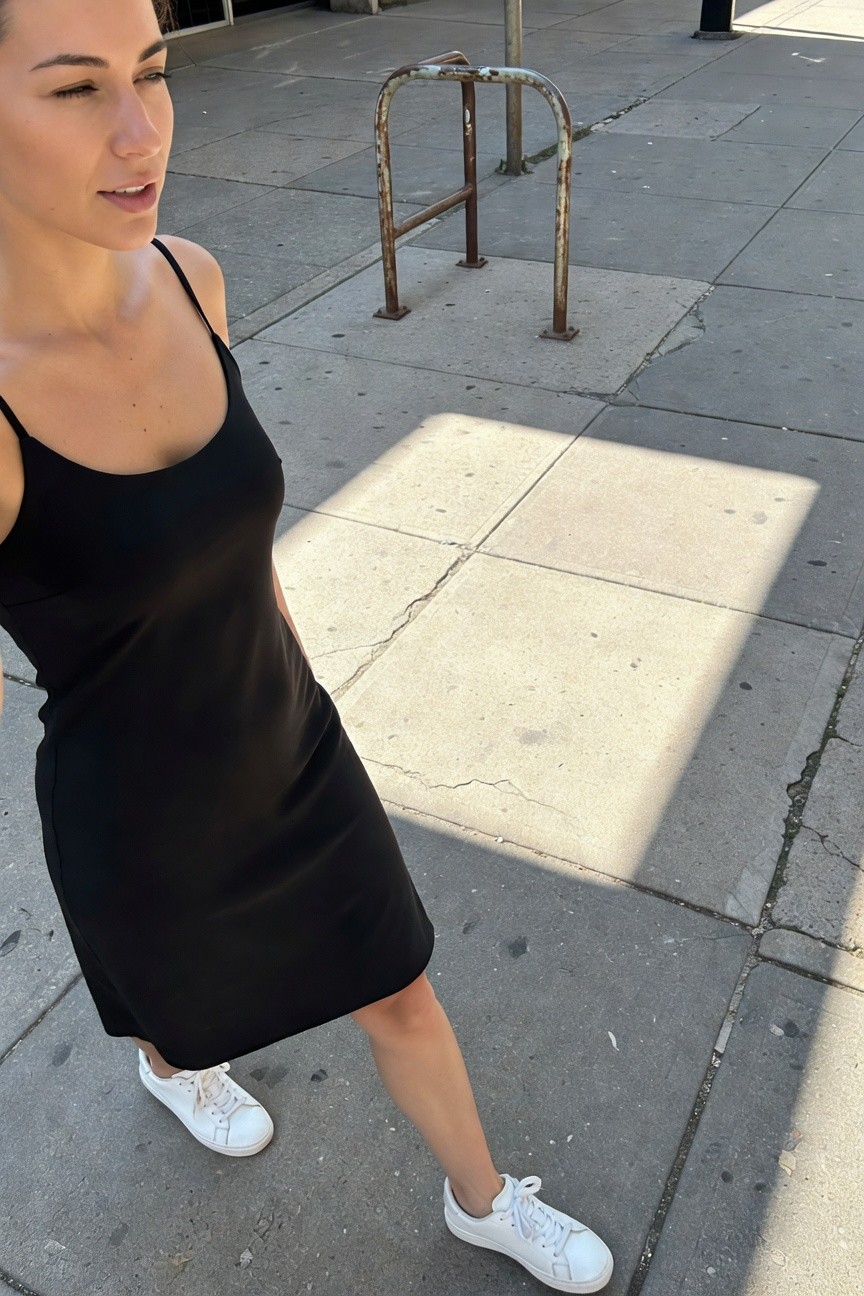 Woman walking on urban sidewalk in black spaghetti-strap slip dress and white platform sneakers, minimalist summer outfit with clean lines and subtle sheen on fabric