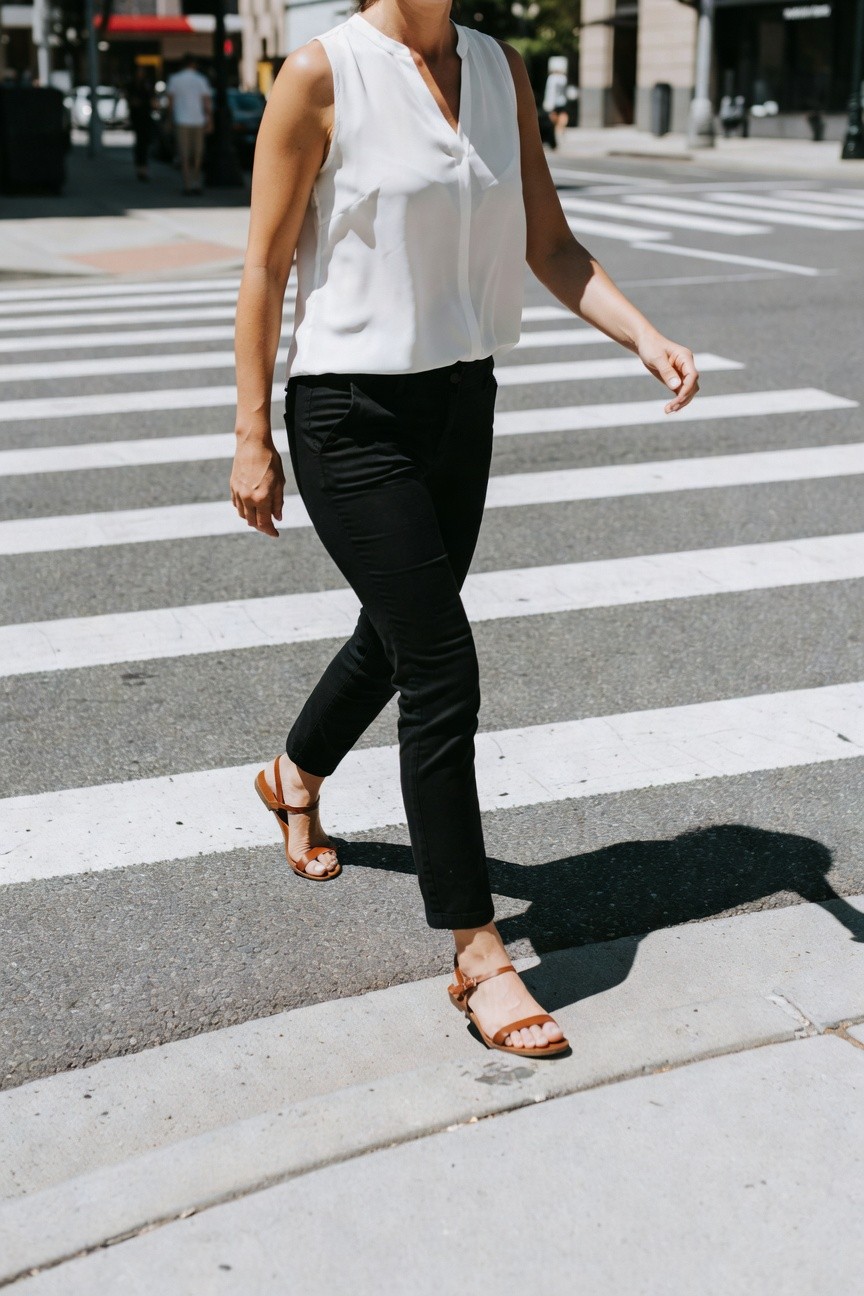Woman walking in white sleeveless blouse tucked into slim black ankle pants and tan strap sandals with low heel
