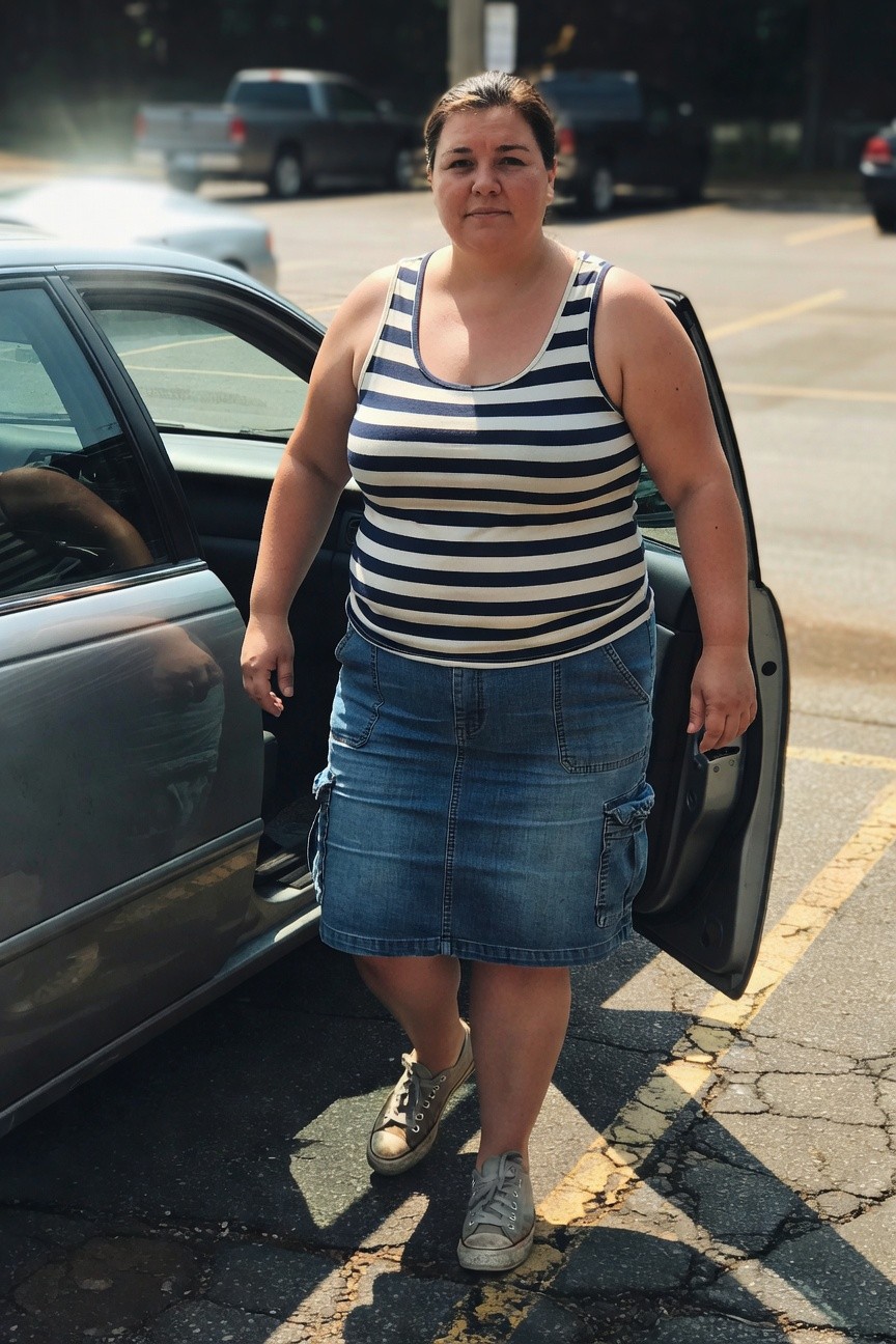Plus-size woman standing by open car door wearing navy and white horizontal striped sleeveless tank top, mid-length blue cargo denim skirt with side pockets, and white Converse-style sneakers on cracked parking lot pavement