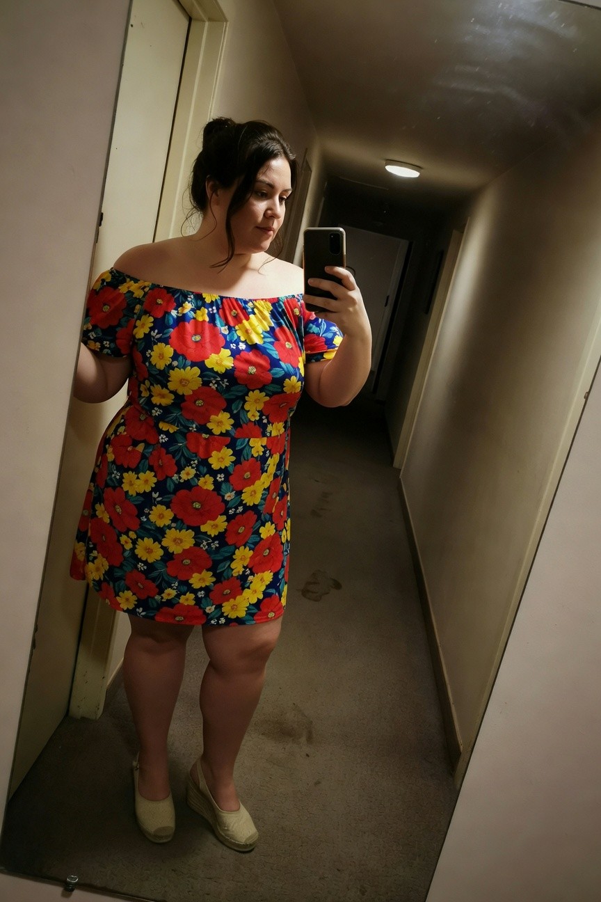 Plus-size woman taking a mirror selfie in a hallway, wearing a colorful off-shoulder floral print dress in red, yellow, and blue with short puffed sleeves and flared skirt, paired with tan espadrille wedge sandals