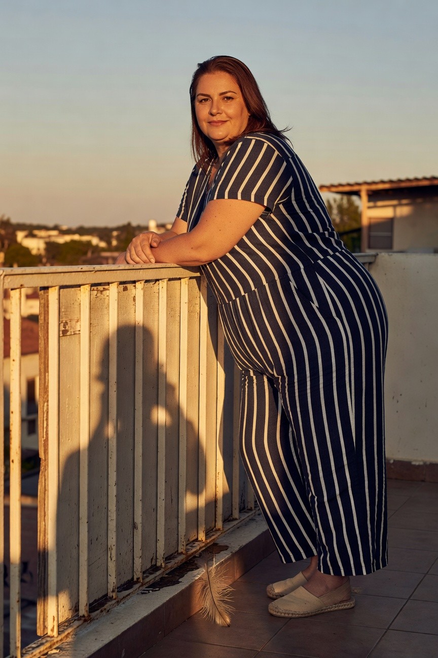 Plus size woman leaning on railing in navy and white vertical striped short sleeve wide leg jumpsuit with tan espadrille platform sandals