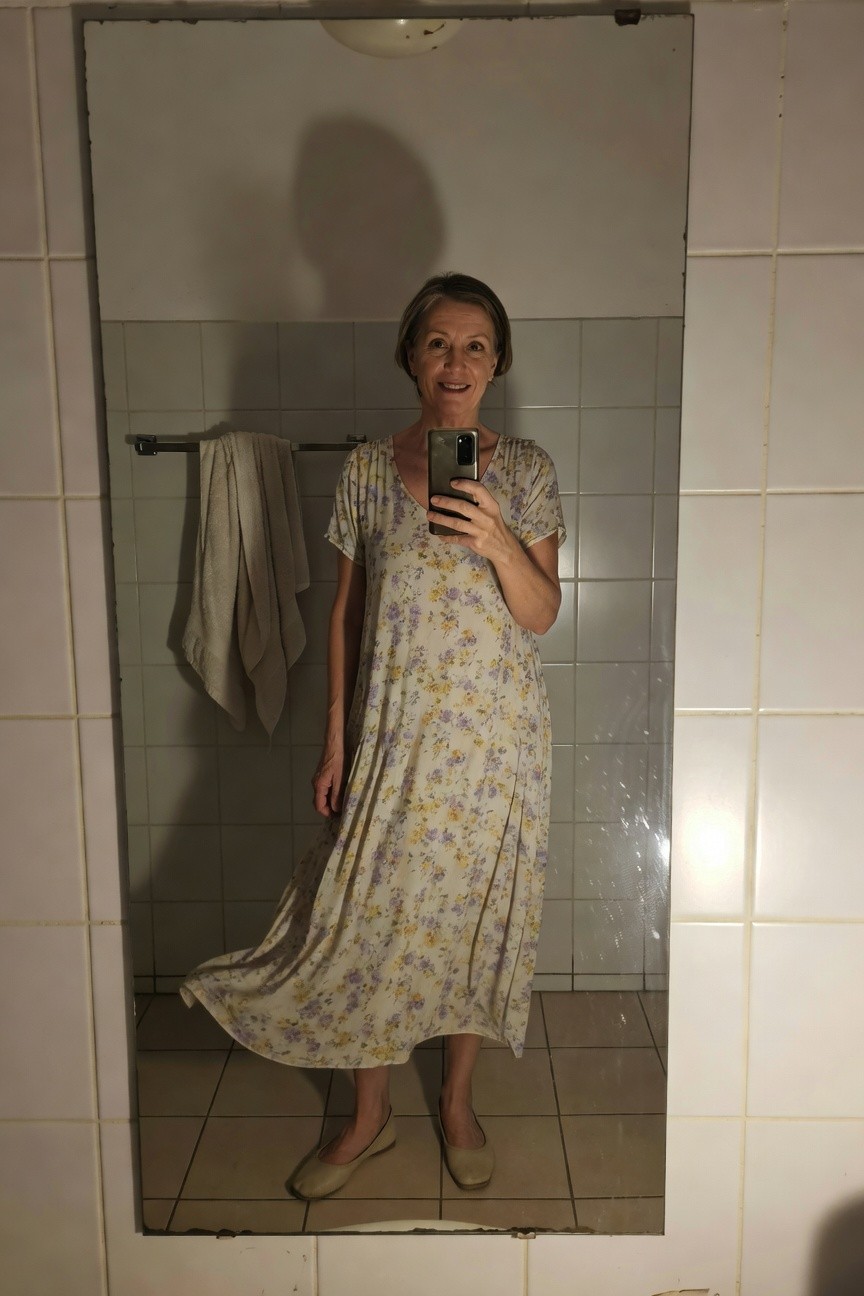 Woman taking a mirror selfie in a bathroom, wearing a lightweight cream floral print midi dress with short sleeves and V-neck, paired with beige ballet flats, smiling at the camera