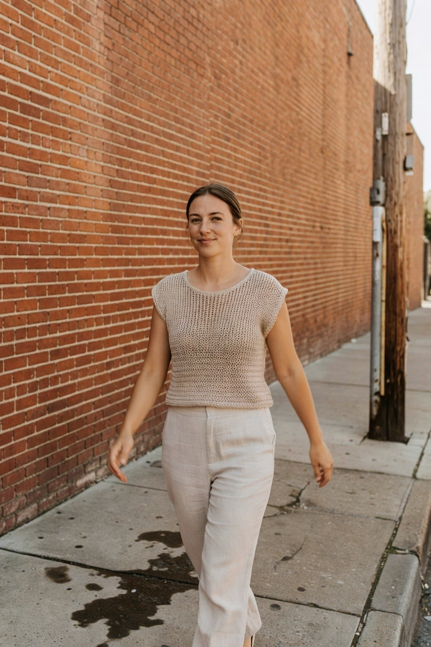Woman in cream open-knit sleeveless top and wide-leg linen pants walking on sidewalk, hands gesturing casually