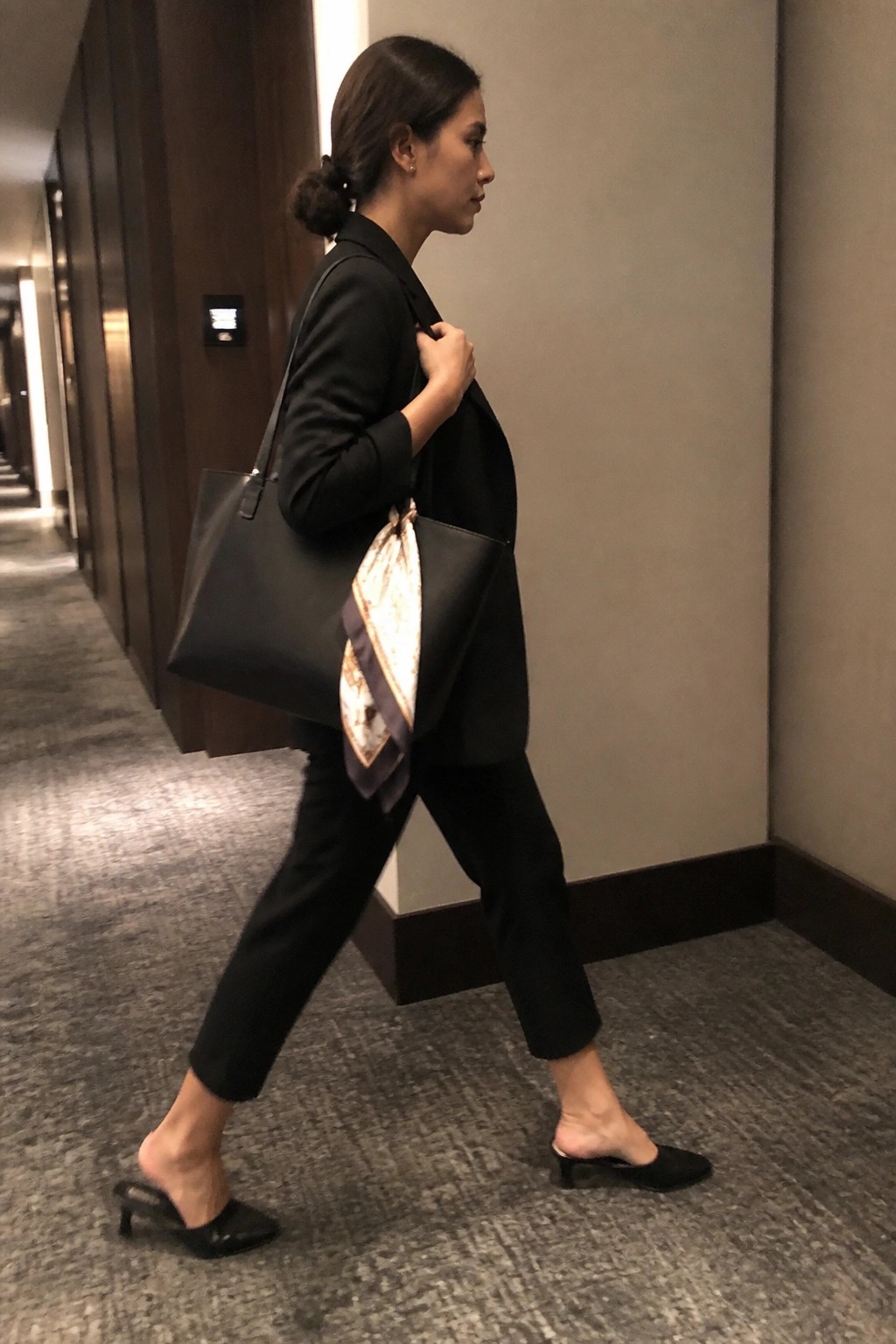 Woman in black blazer carrying large tote bag with scarf in hallway