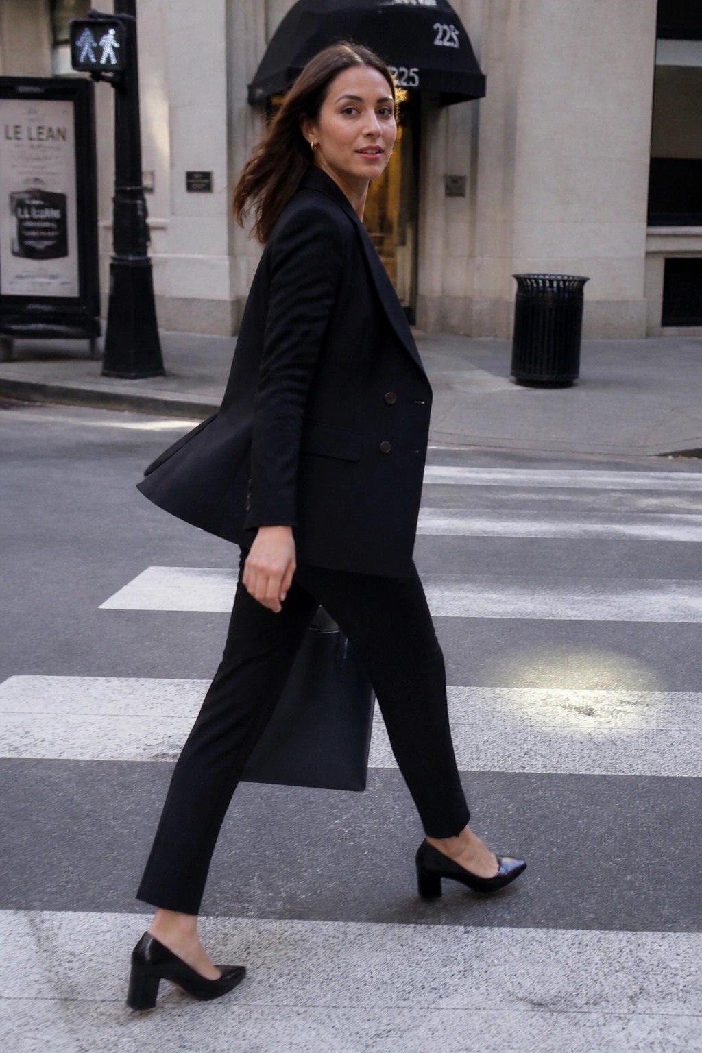 Woman in black suit crossing crosswalk while glancing over shoulder
