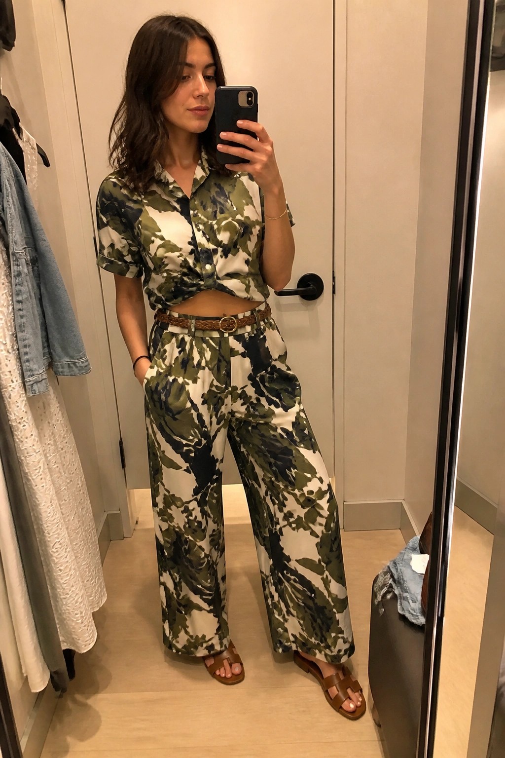 Woman in green camouflage tied shirt and wide pants taking mirror selfie