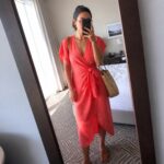 Woman wearing a coral linen wrap midi dress with short sleeves and side knot tie, paired with brown leather flat sandals and a woven straw tote bag, shown in a mirror selfie inside a hotel room.