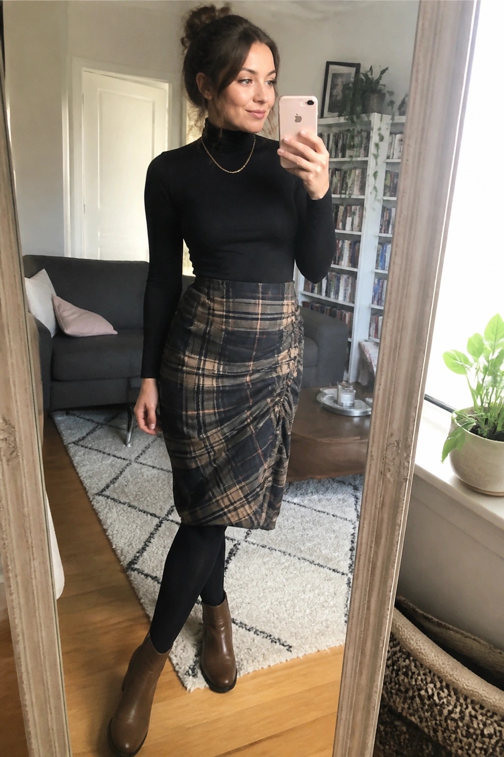 Woman in black turtleneck and plaid skirt taking mirror selfie in living room