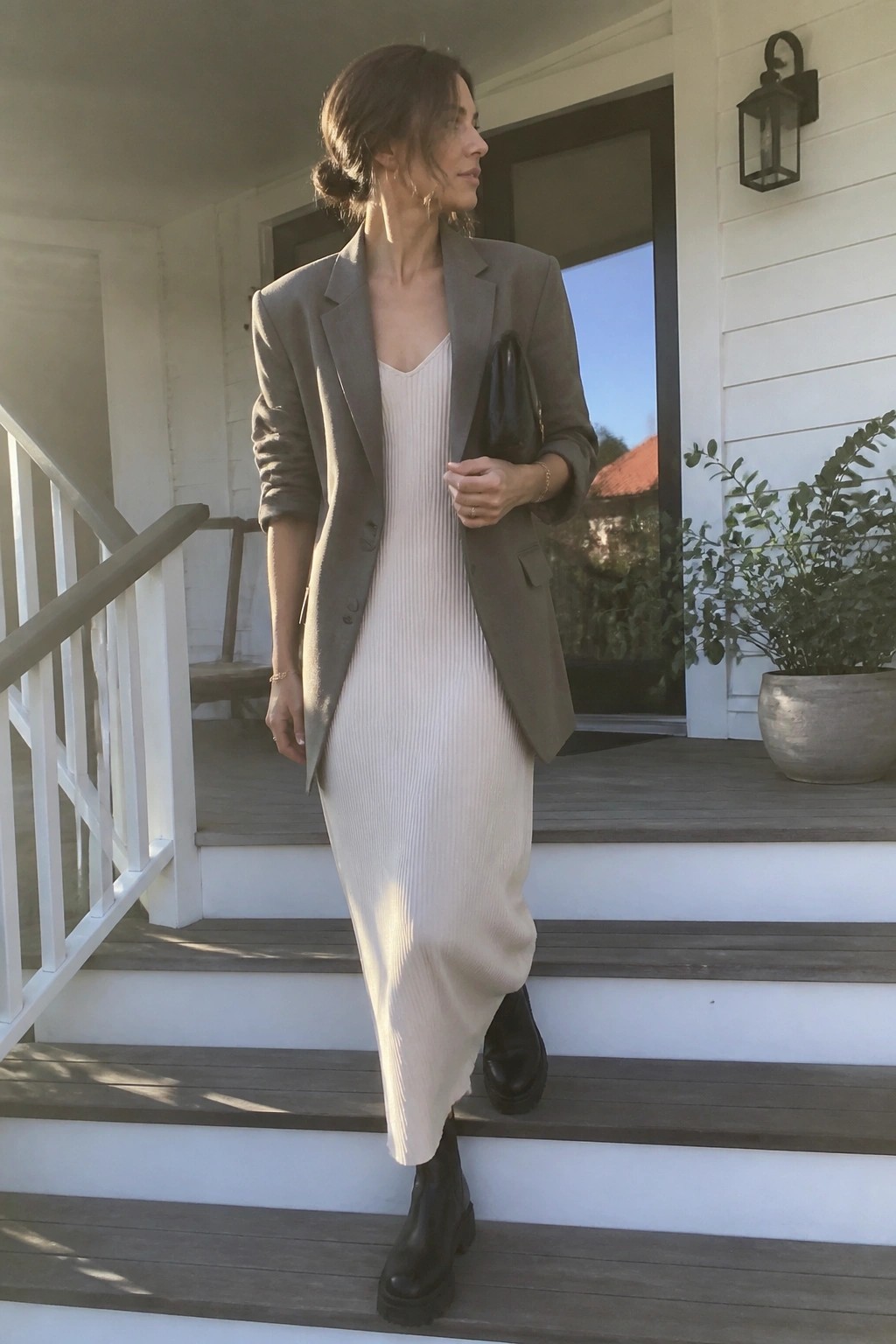 Woman in gray blazer over cream ribbed dress on wooden porch steps with black boots