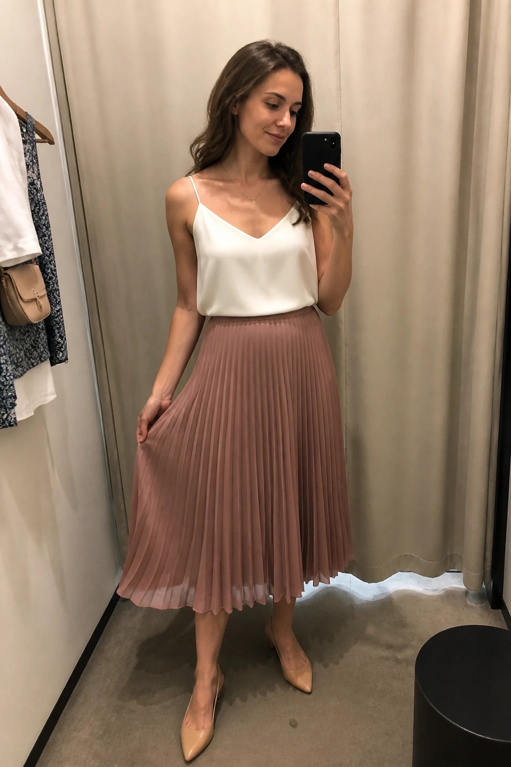 Woman in white camisole and pleated mauve skirt taking mirror selfie in fitting room