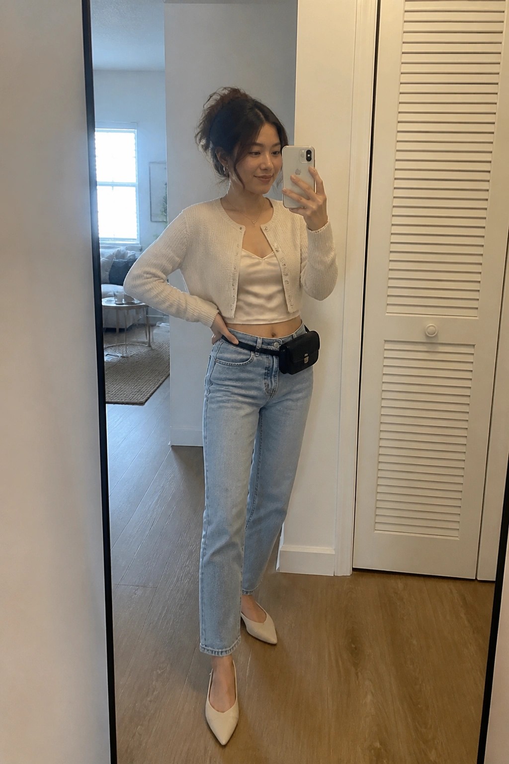 Woman in white cardigan and jeans taking mirror selfie with phone