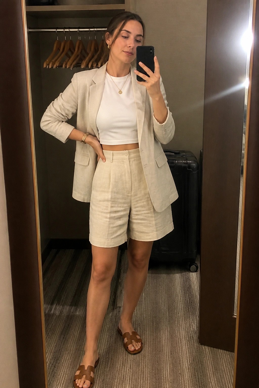 Woman in beige linen blazer and shorts taking mirror selfie with phone