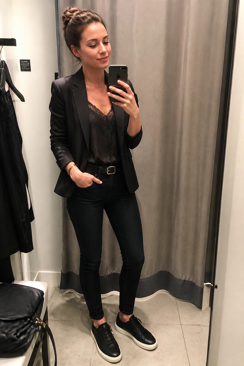 Woman in black blazer and lace top taking mirror selfie in fitting room