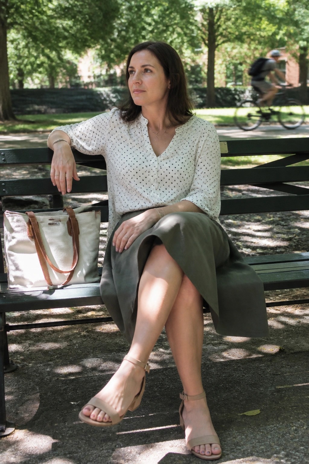 Woman in polka-dot blouse and green skirt on park bench with tote bag