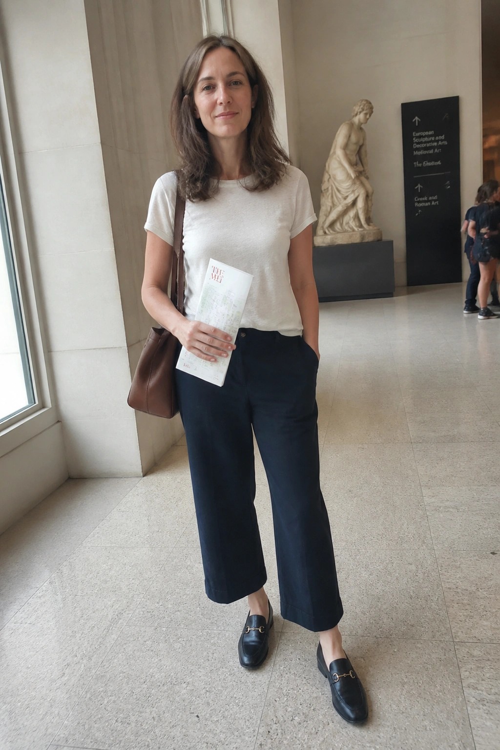 Woman in white t-shirt and navy pants holding The Met map in museum