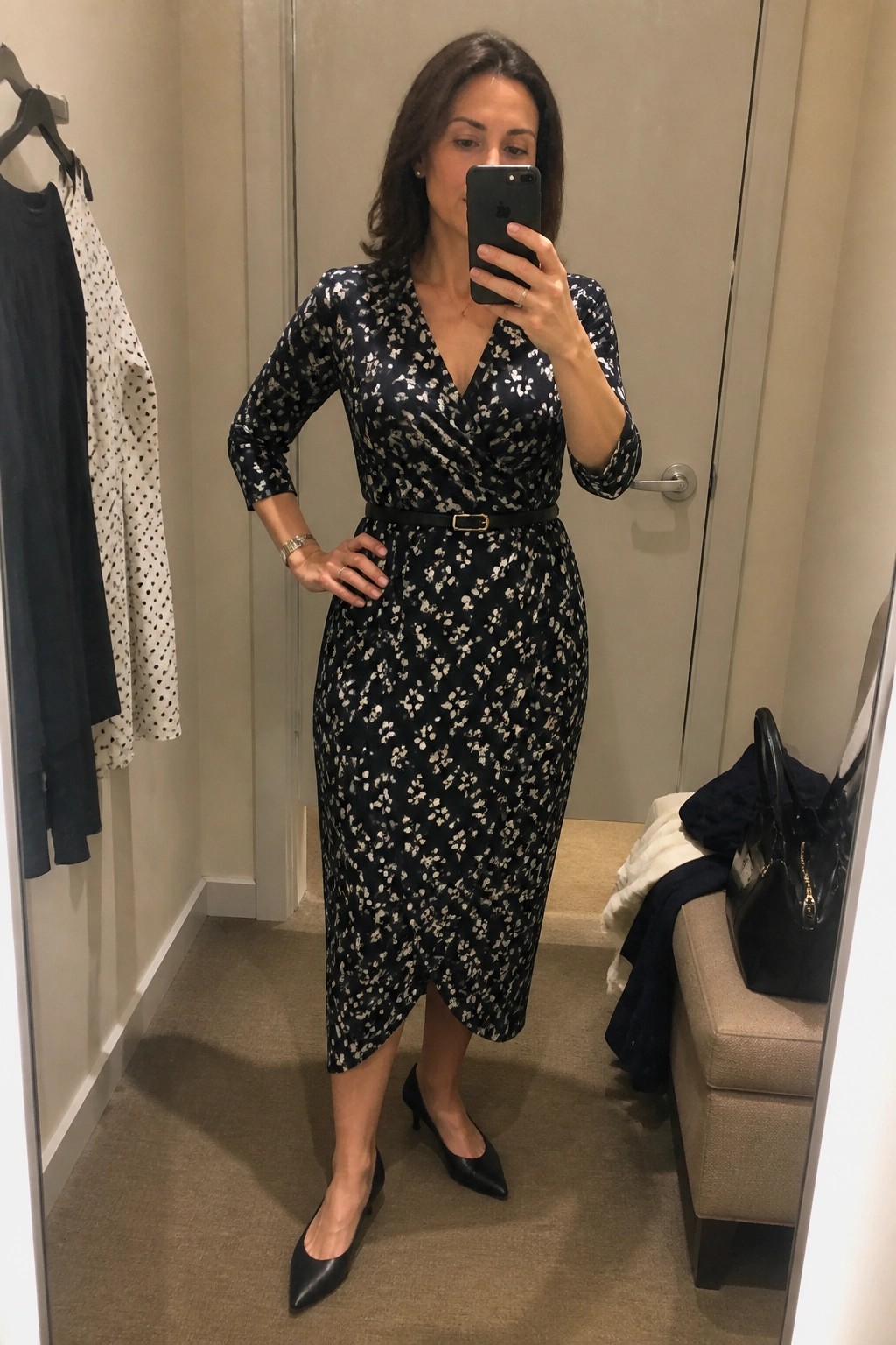 Woman in black floral wrap dress taking mirror selfie in fitting room
