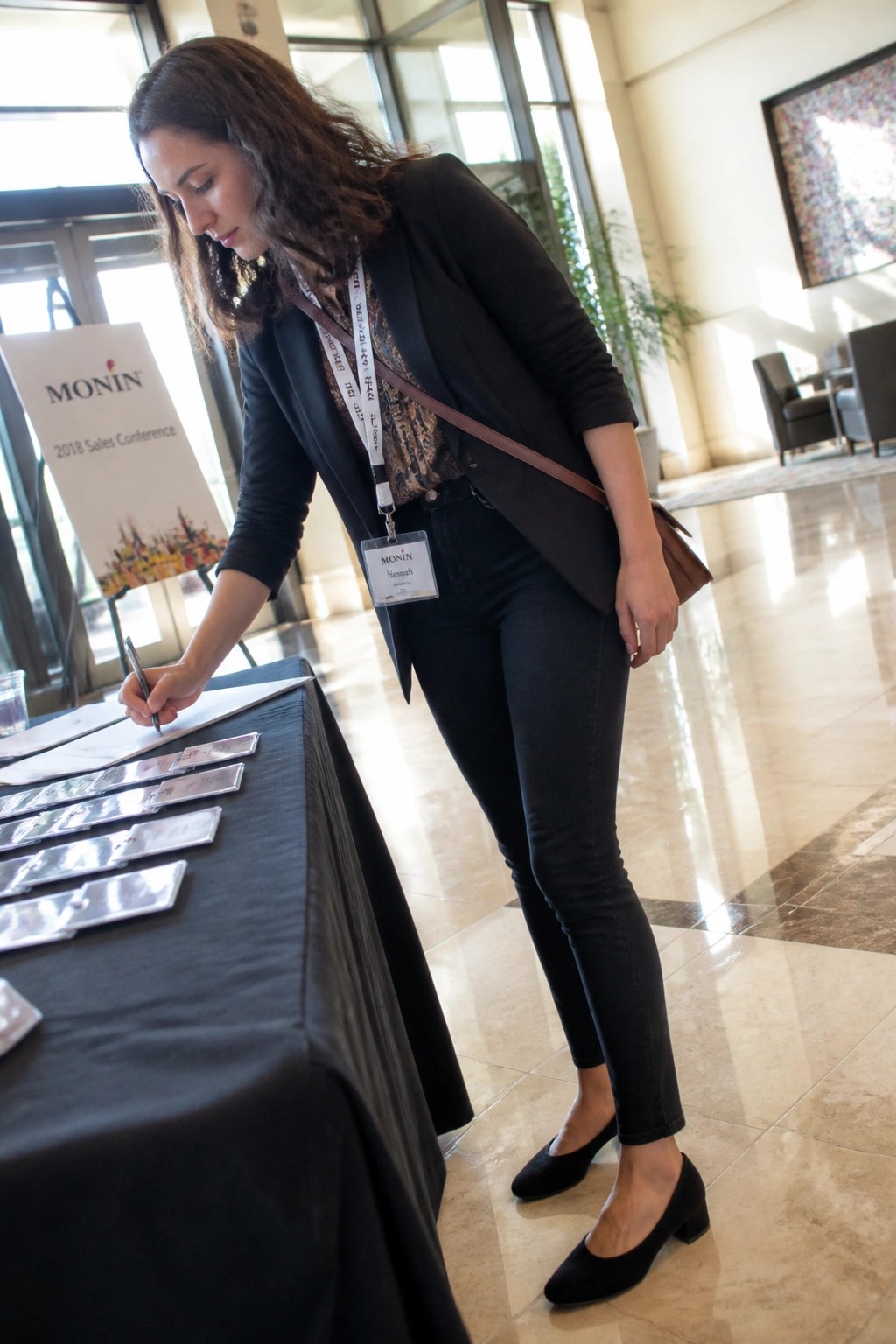 Woman in black blazer signs papers at Monin conference registration table