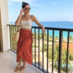 Woman in cream crochet top and rust wrap skirt on ocean-view balcony