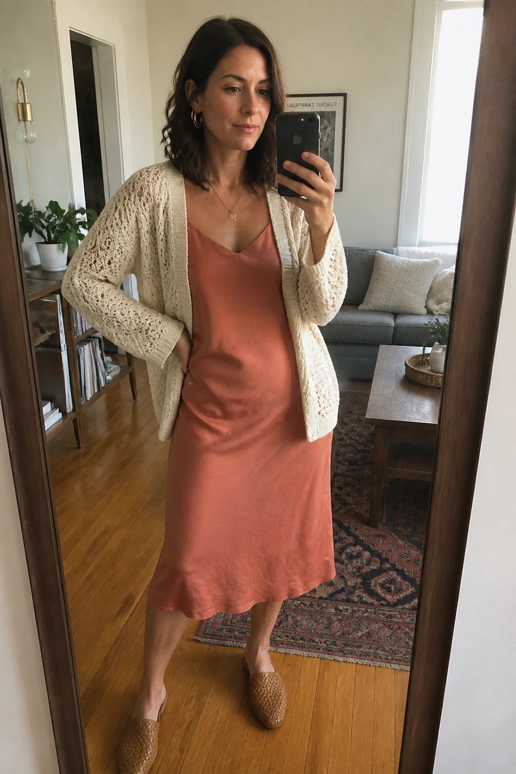 Woman in rust midi slip dress layered under cream open knit cardigan with woven mules and delicate gold necklace shown in mirror selfie