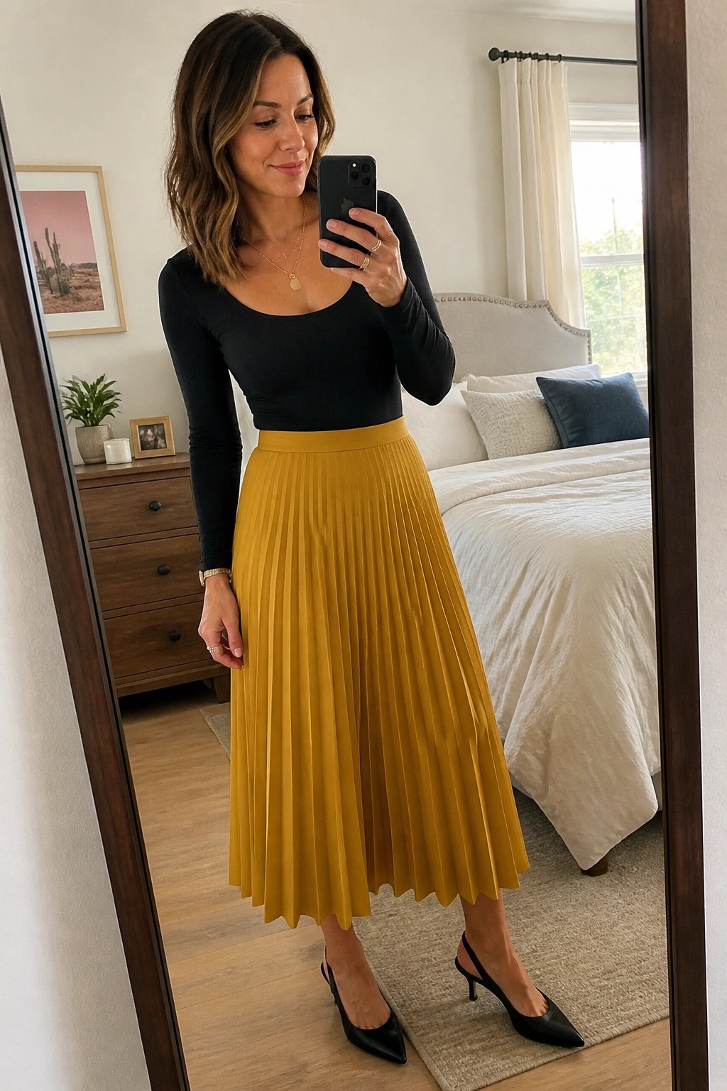 Woman in black top and mustard-yellow pleated skirt taking bedroom mirror selfie