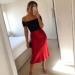 Woman in black off-shoulder top and red satin skirt taking bedroom mirror selfie