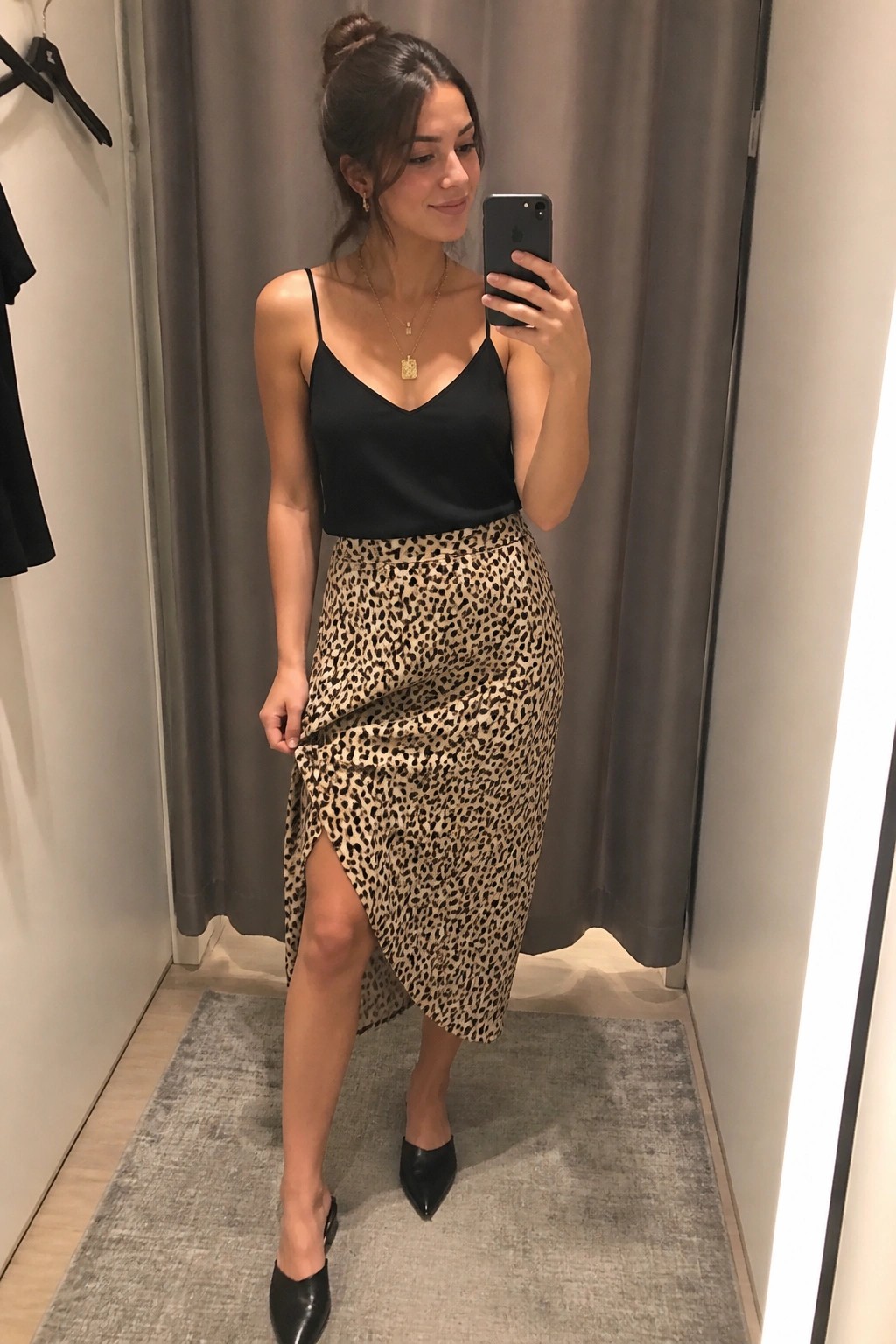Woman in mirror selfie wearing black camisole top with thin straps, leopard print midi skirt featuring side slit, black pointed toe mules, and layered gold necklaces.