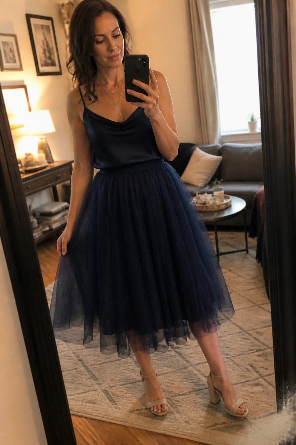 Woman in navy satin camisole and tulle skirt takes living room mirror selfie