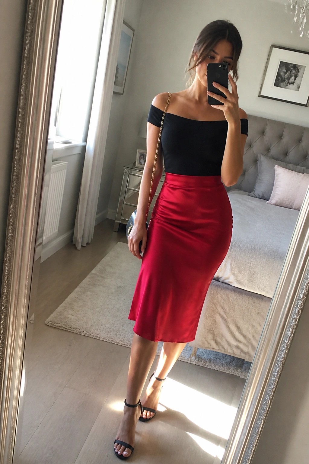 Woman in black off-shoulder top and red satin skirt taking bedroom mirror selfie