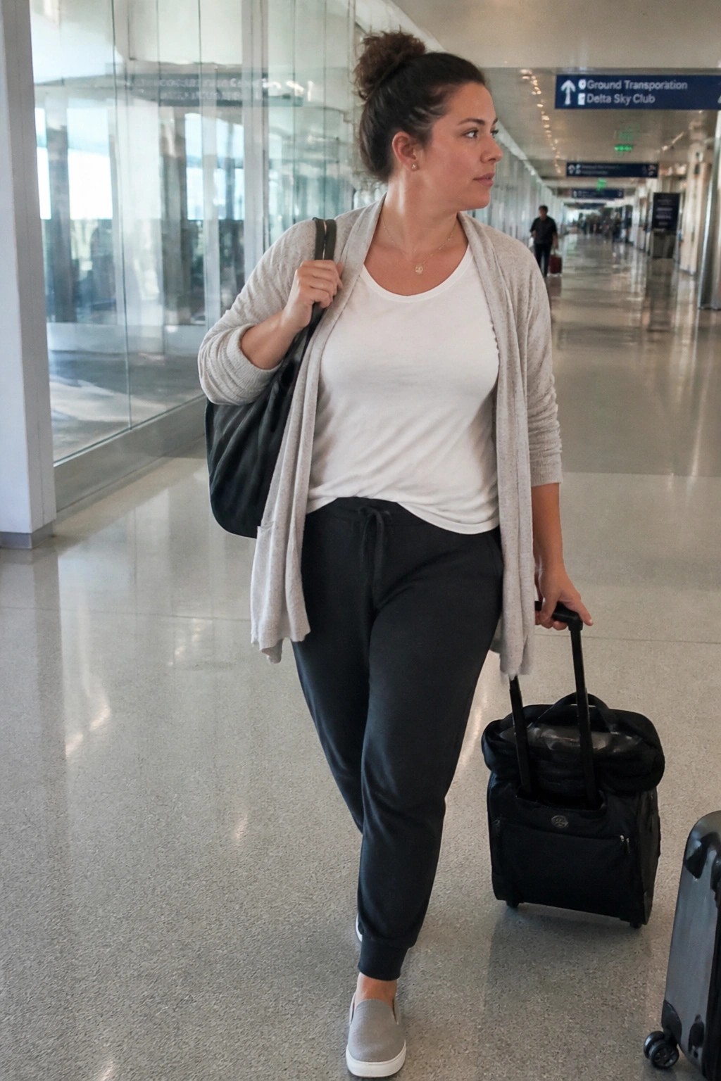 Woman in white top and gray cardigan pulls black suitcase through airport terminal