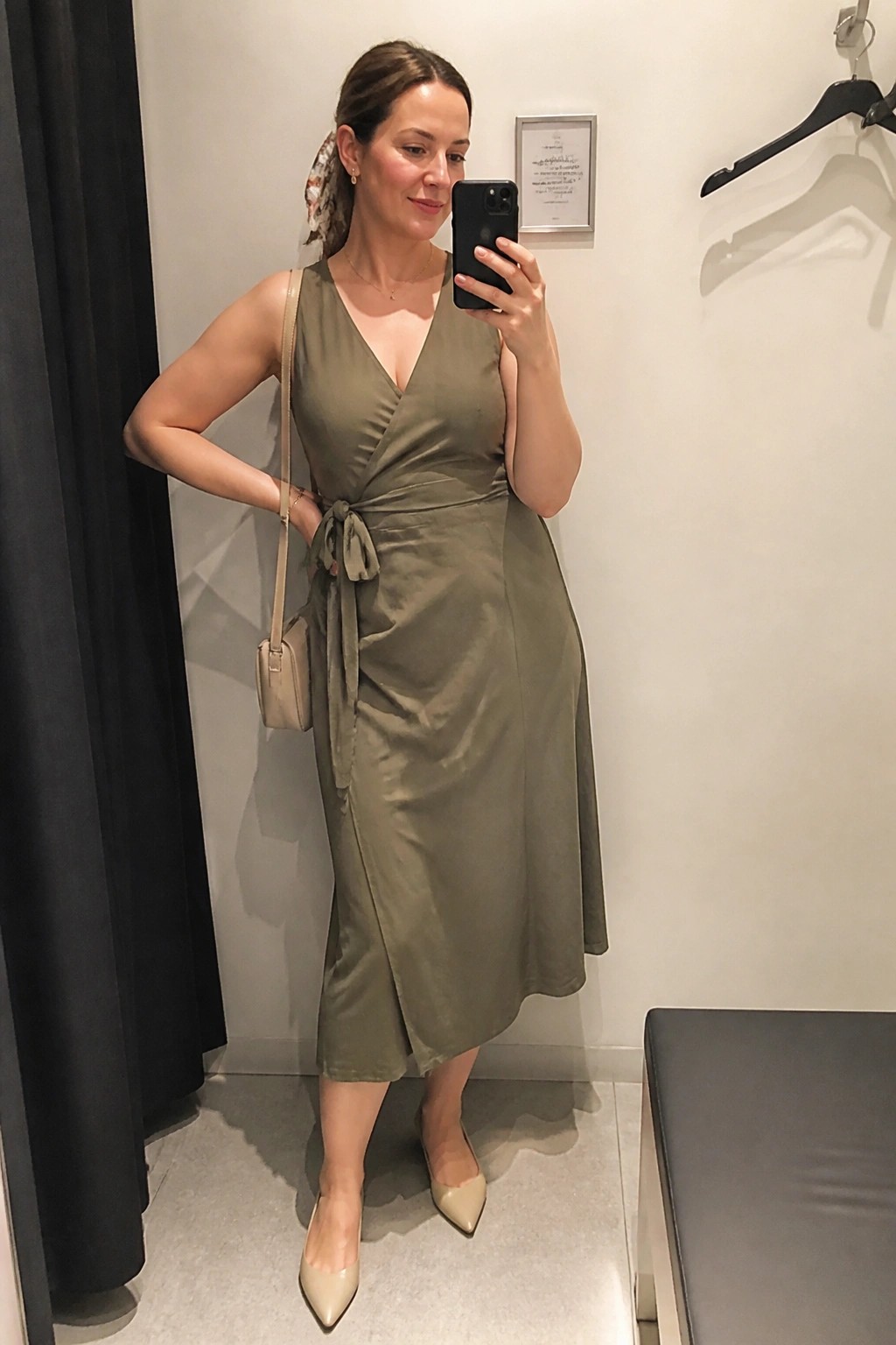 Woman in olive wrap dress taking mirror selfie in fitting room