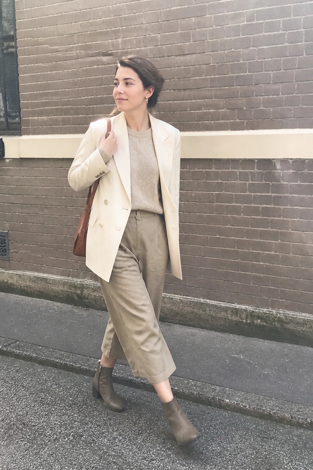 Woman in cream blazer and beige pants with brown bag on city street