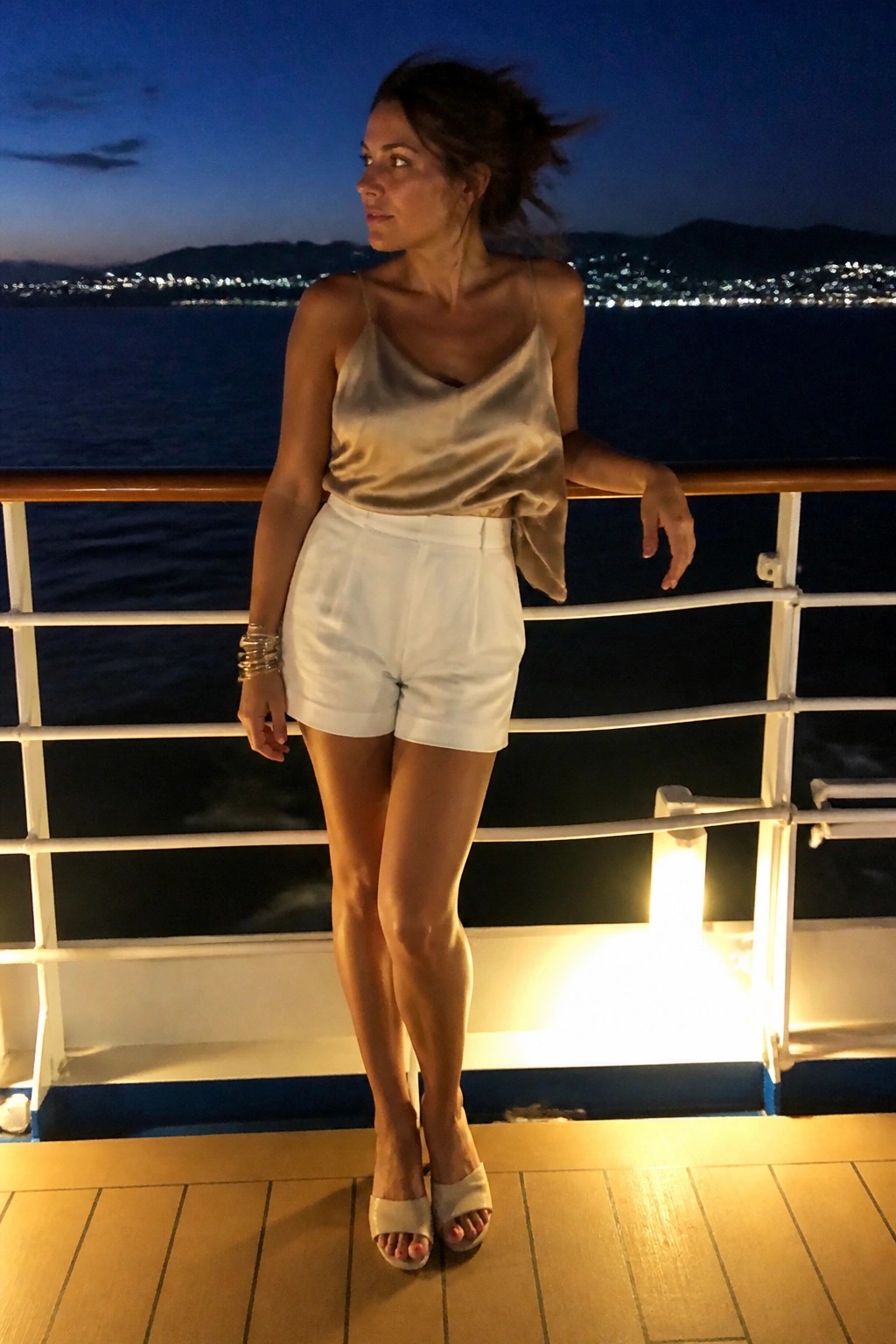 Woman in satin camisole and white shorts leaning on ship railing at night
