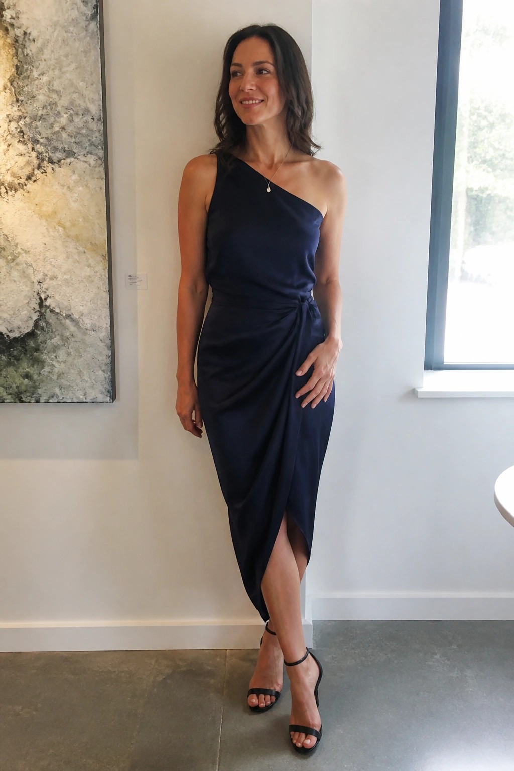 Woman in navy one-shoulder midi dress with side knot and black heels