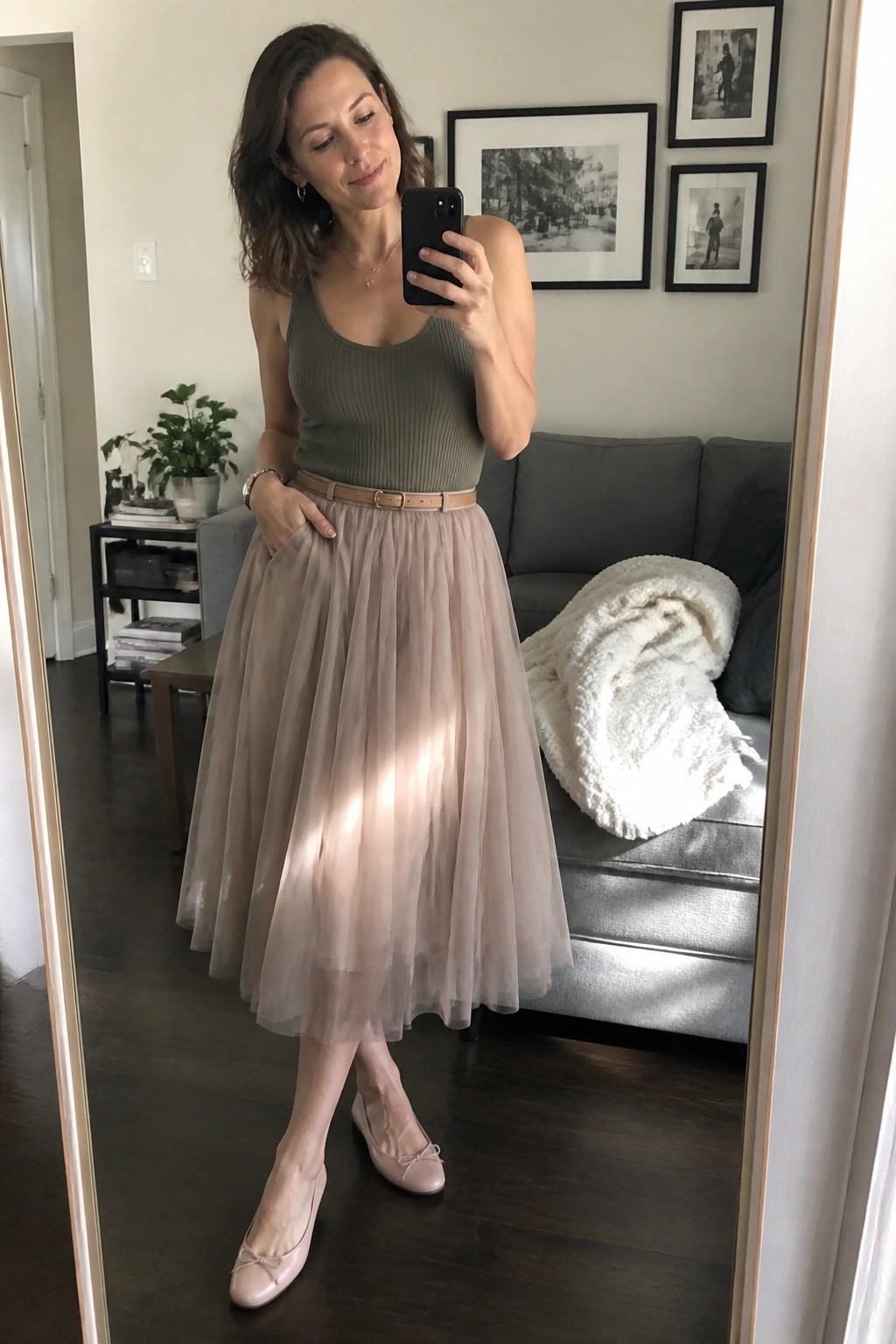 Woman in green tank top and beige tulle skirt taking mirror selfie in living room