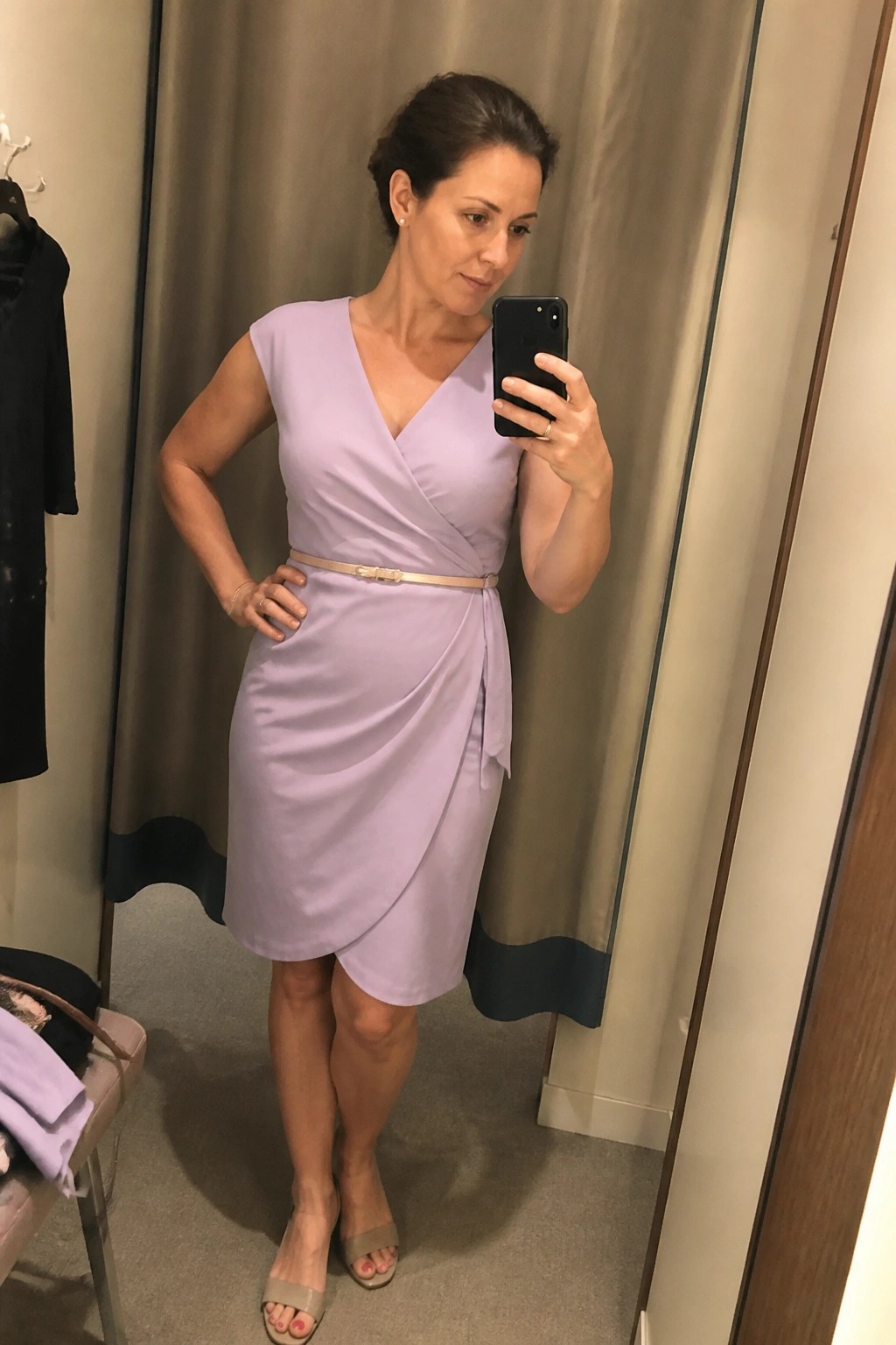 Woman in lavender wrap dress with gold belt taking mirror selfie in fitting room