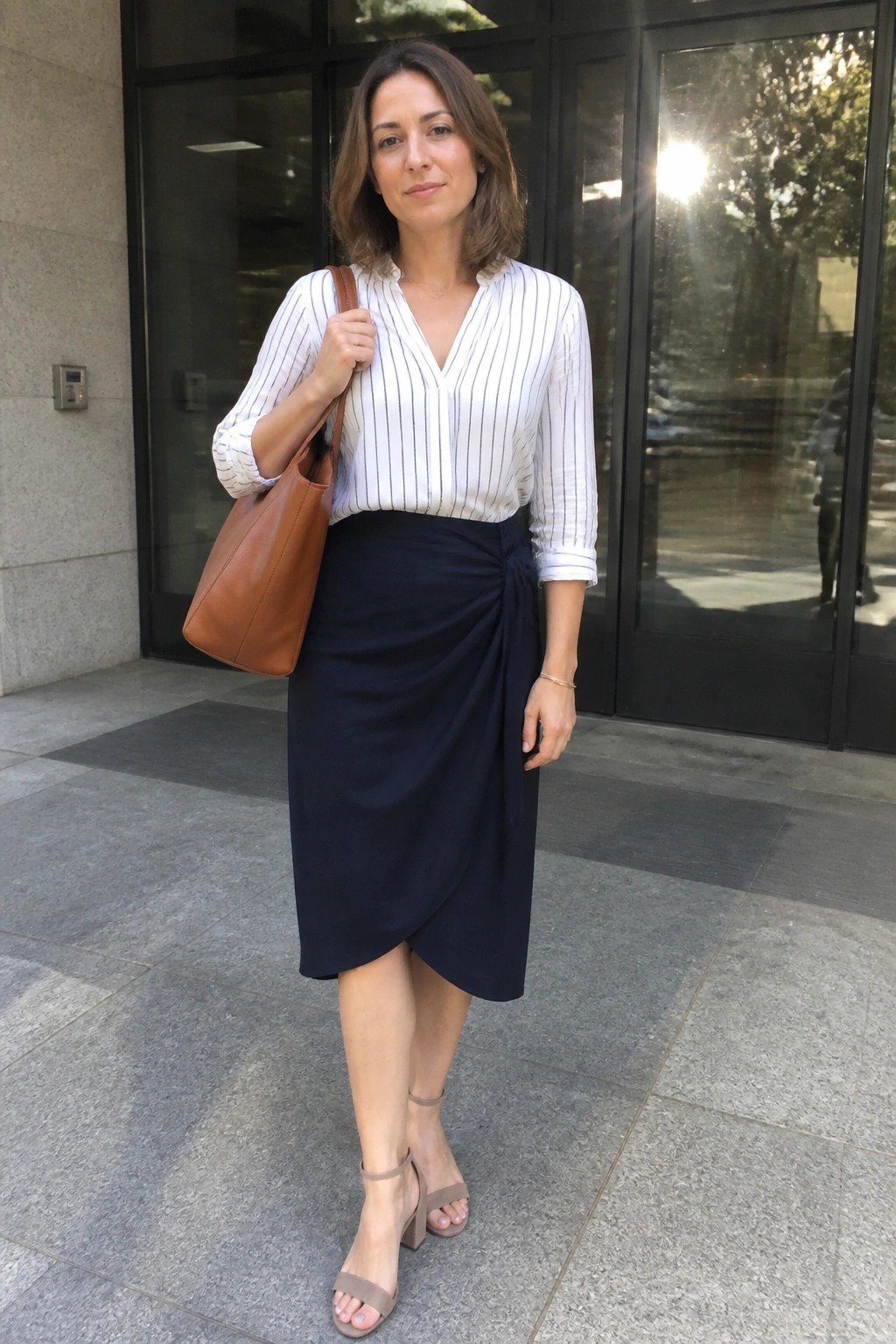 Woman in white striped blouse and navy wrap skirt holding brown leather tote bag