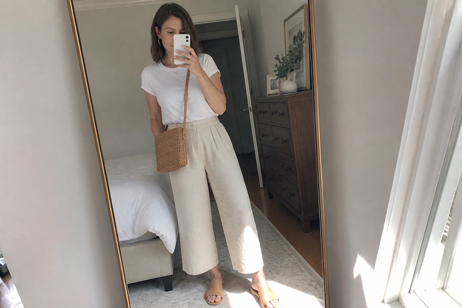 Woman in white tee and beige wide-leg pants taking bedroom mirror selfie