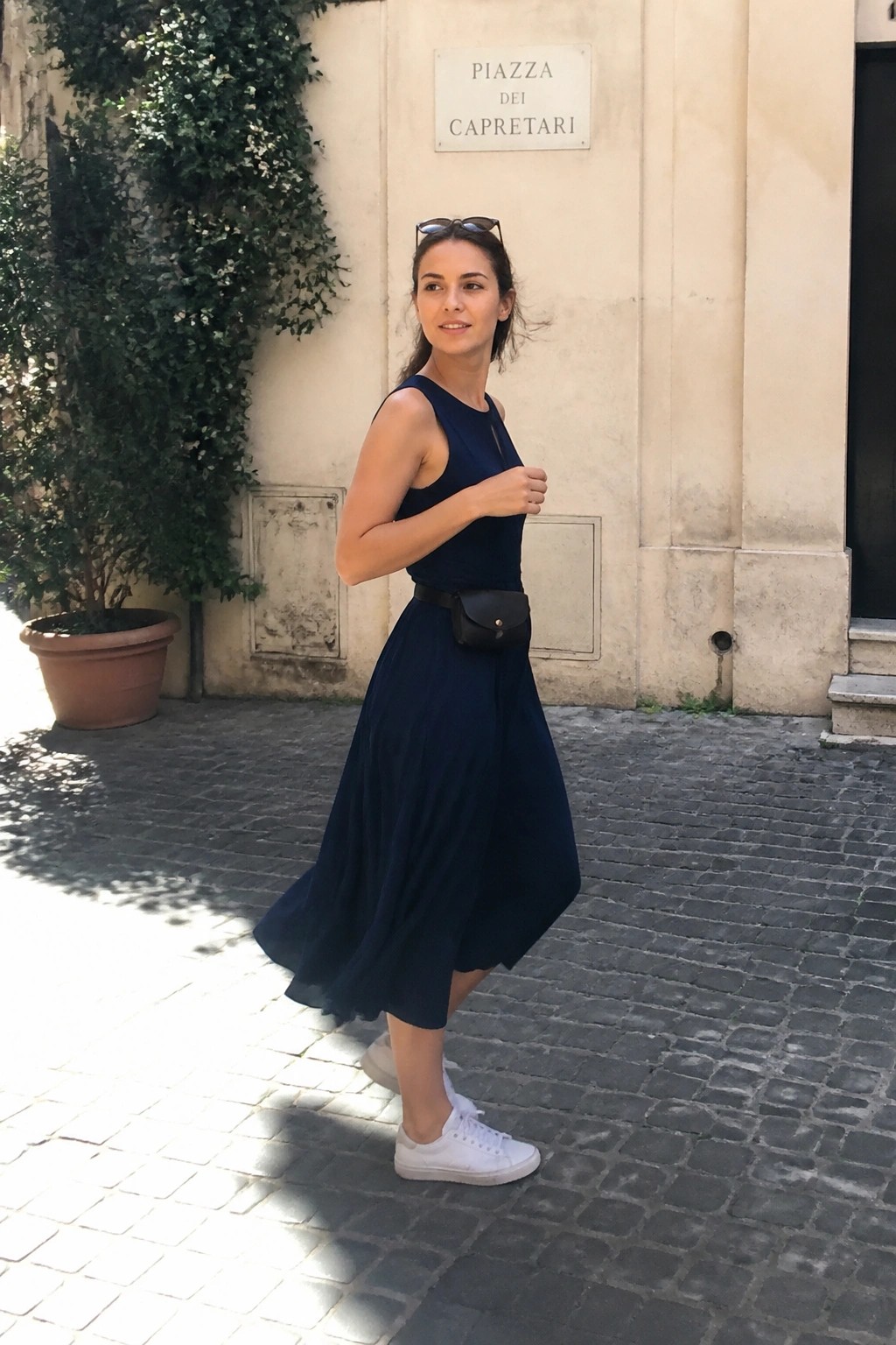 Woman in navy dress with white sneakers on cobblestone street by piazza sign.