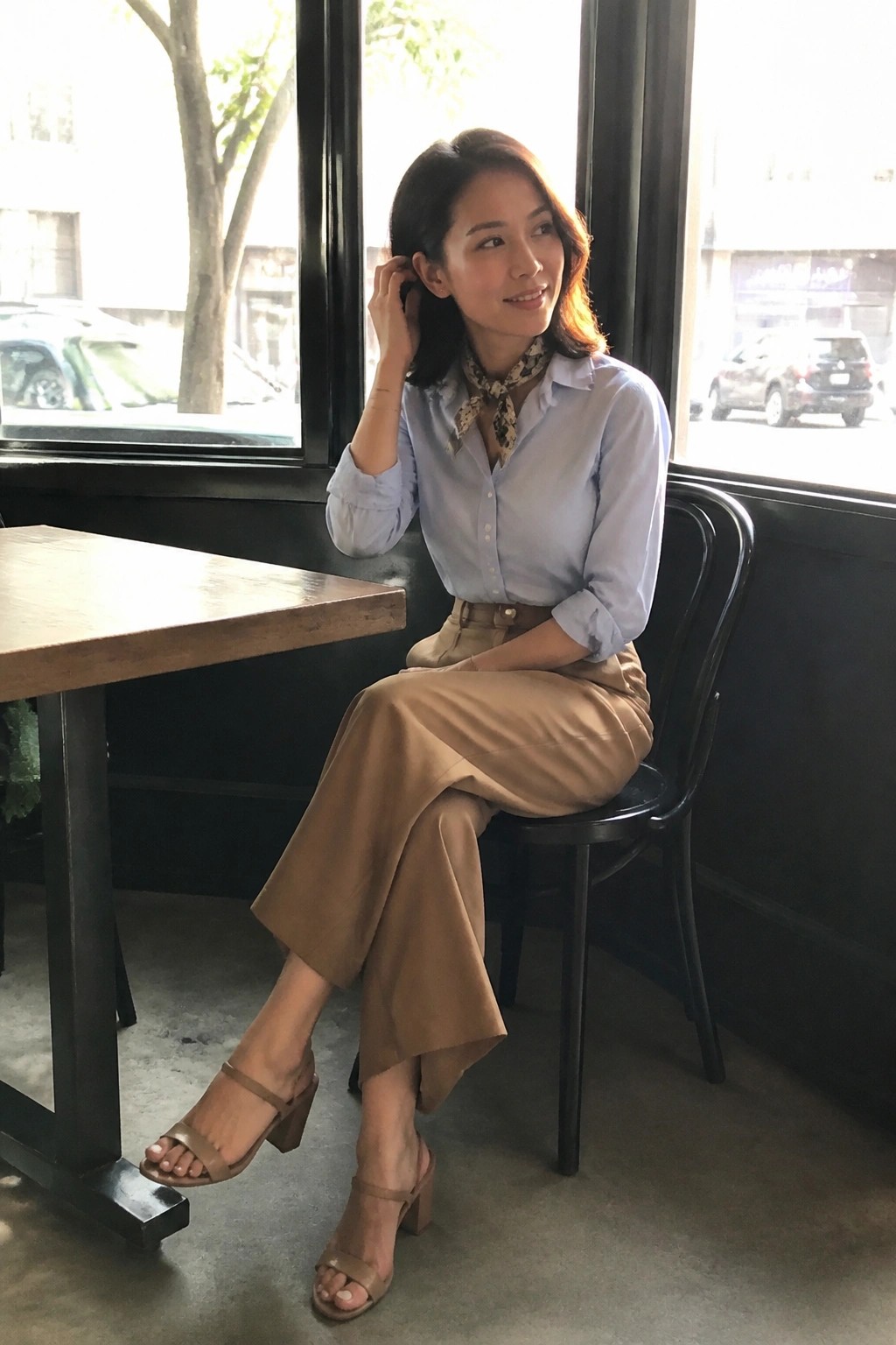 Woman in blue shirt and beige pants seated by window in cafe