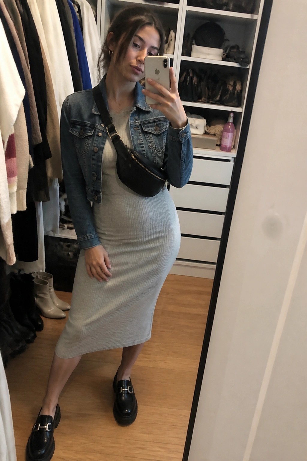Woman in denim jacket and gray midi dress taking mirror selfie in closet