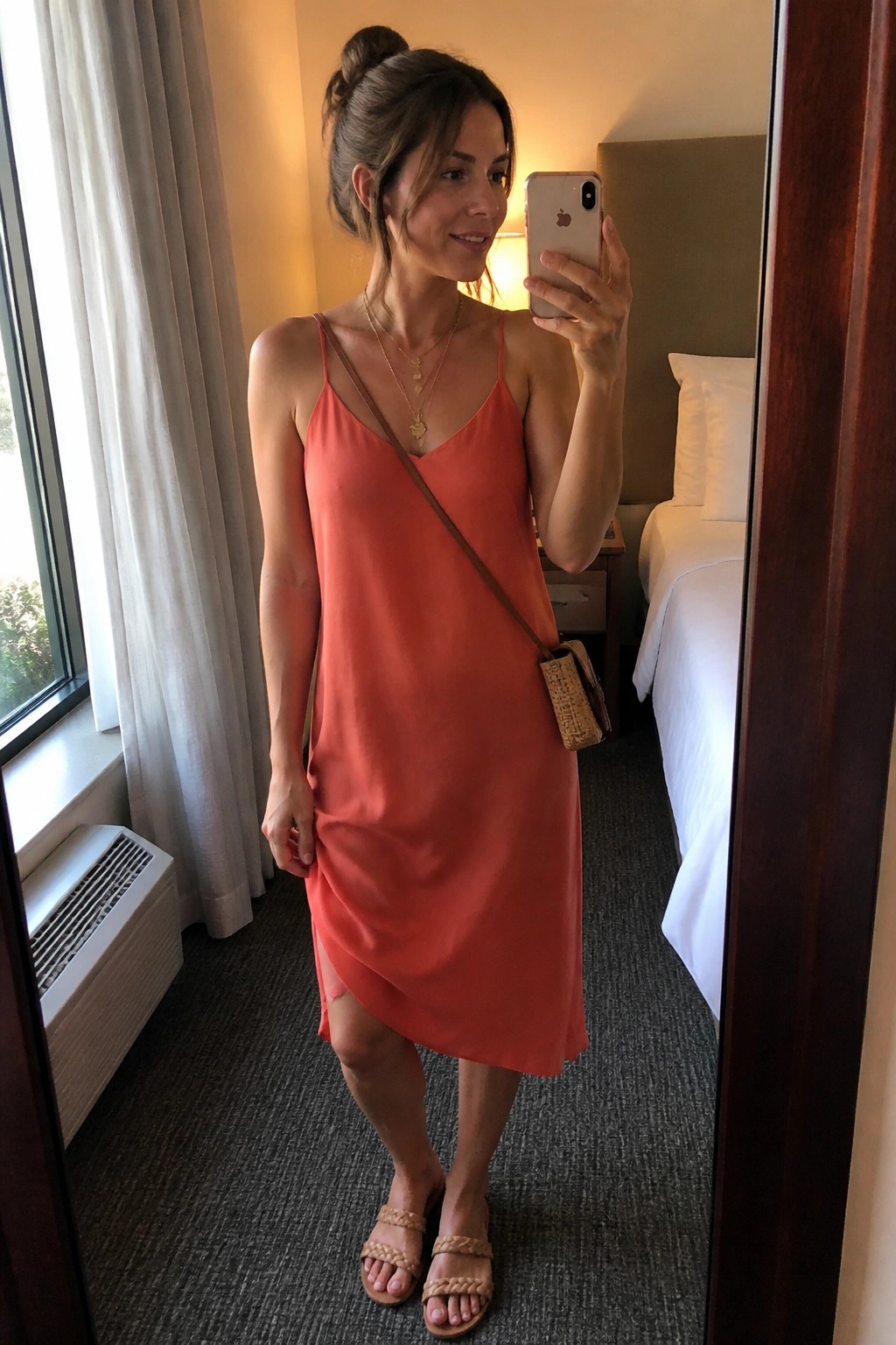 Woman in coral slip dress taking mirror selfie in hotel room with phone