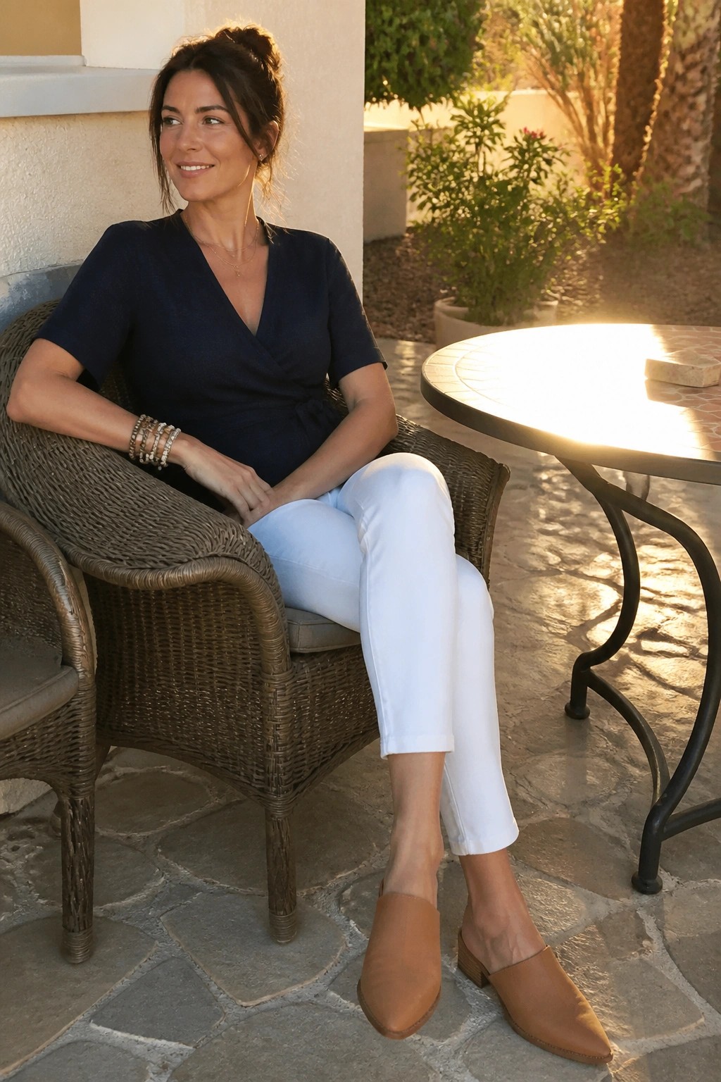 Woman in navy top and white pants seated in outdoor wicker chair
