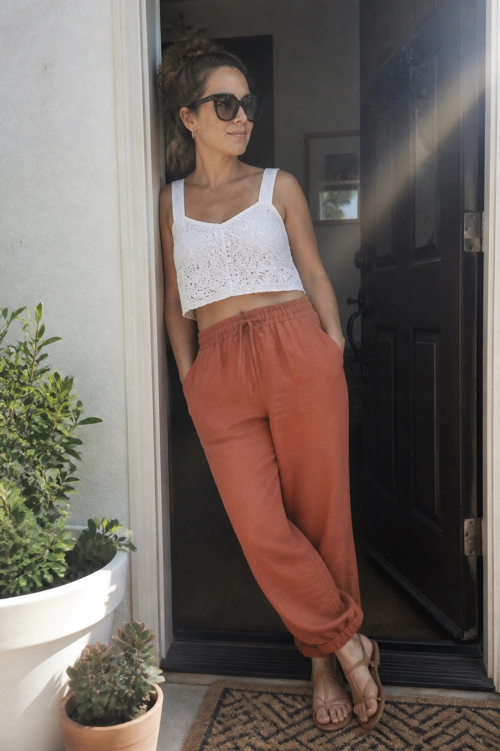 Woman in white lace crop top and orange pants standing in sunny doorway