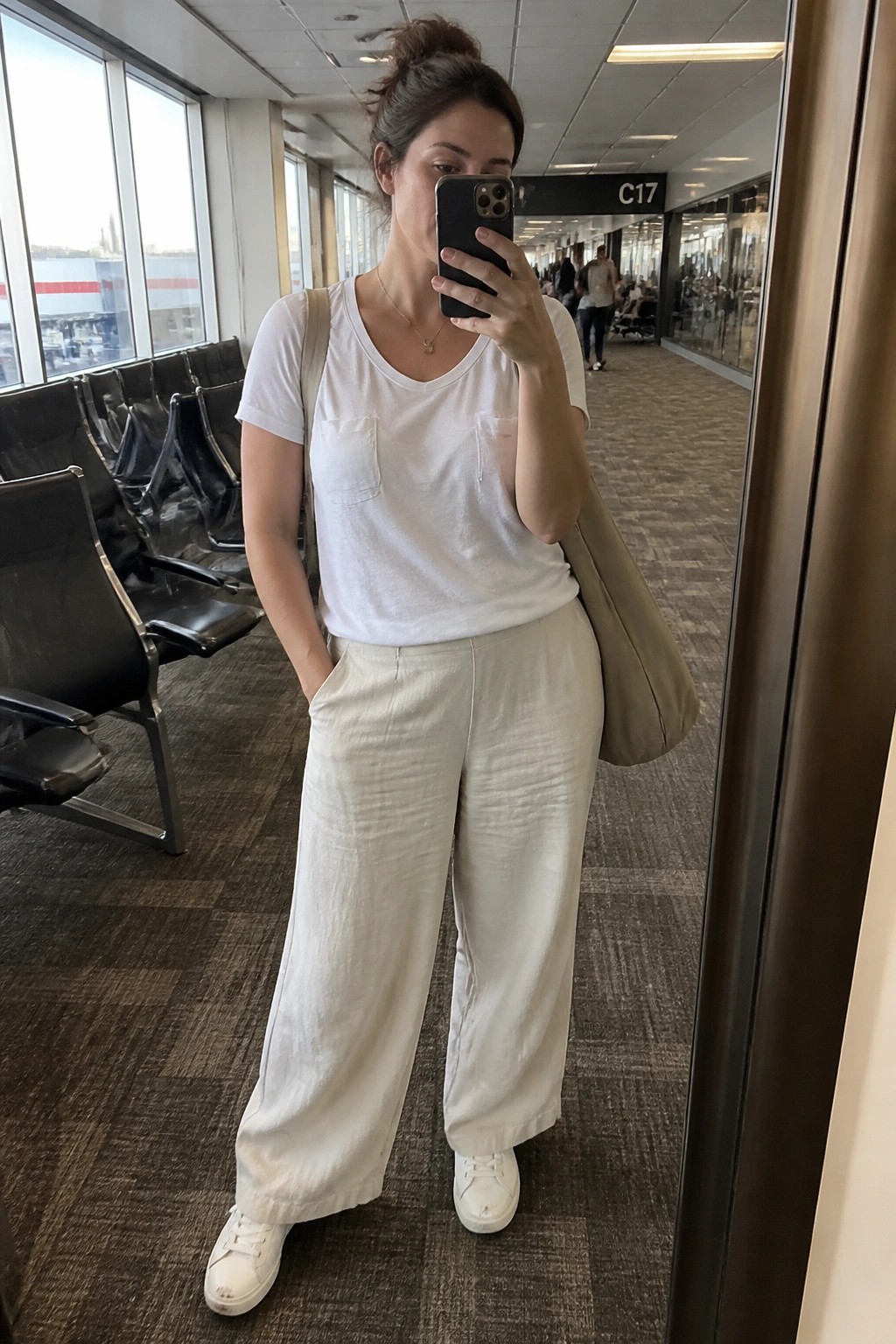 Woman in white tee and wide pants taking mirror selfie at airport gate