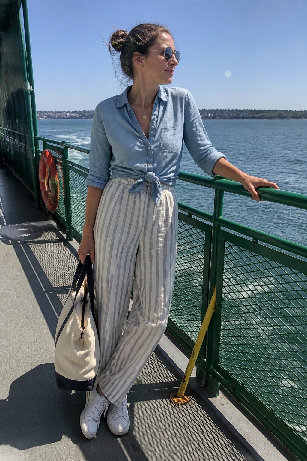 Woman in blue tied shirt and striped pants on sunny boat deck railing