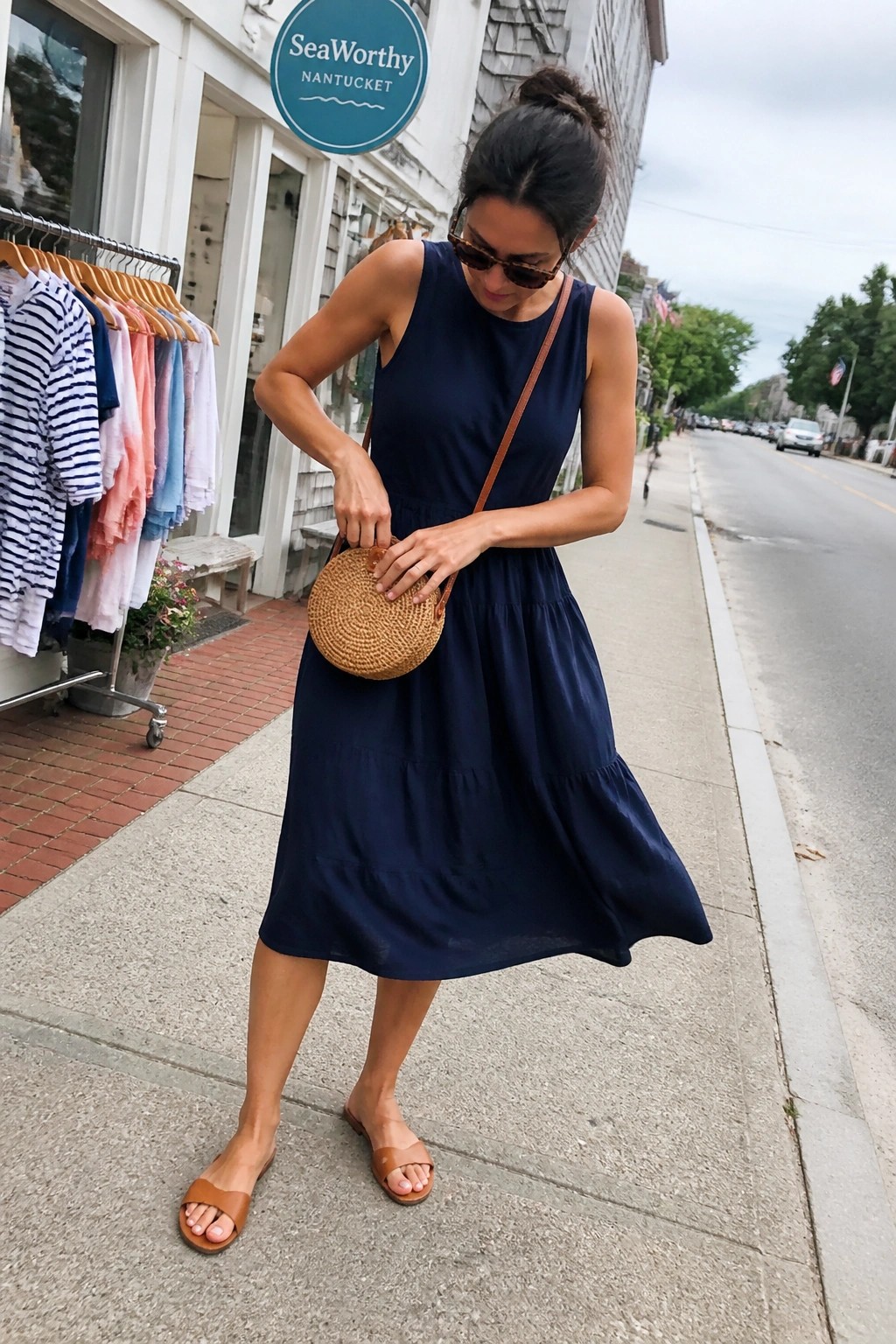 Woman in navy tiered dress with round woven bag on Nantucket sidewalk