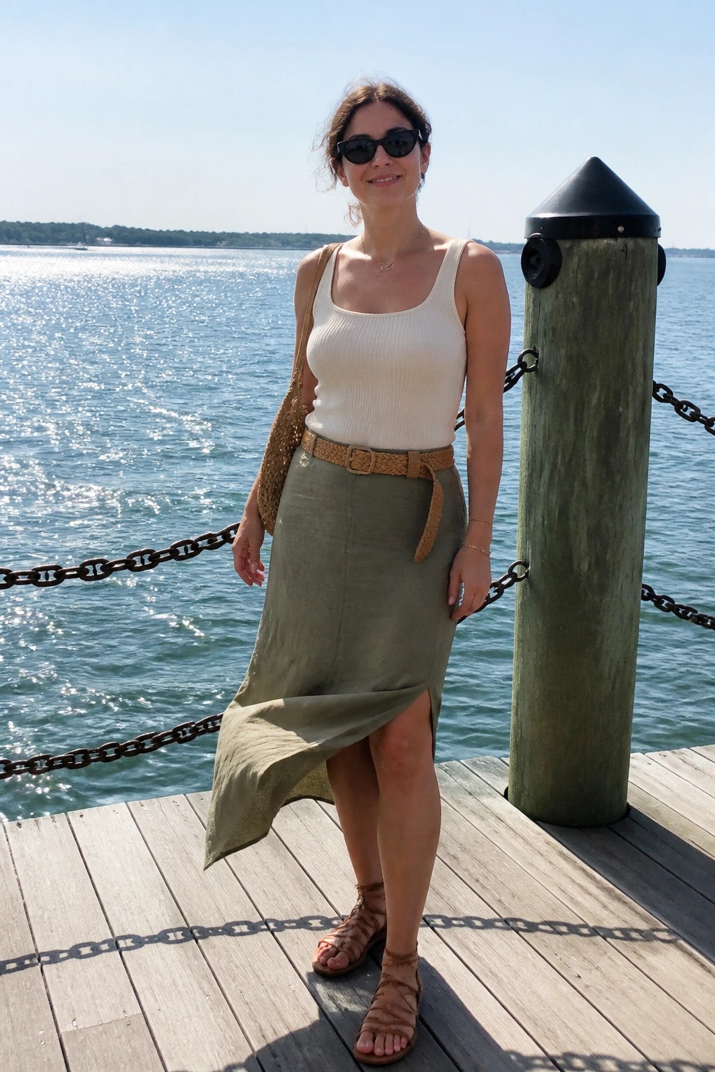 Woman in white top and olive skirt on sunny dock by water.