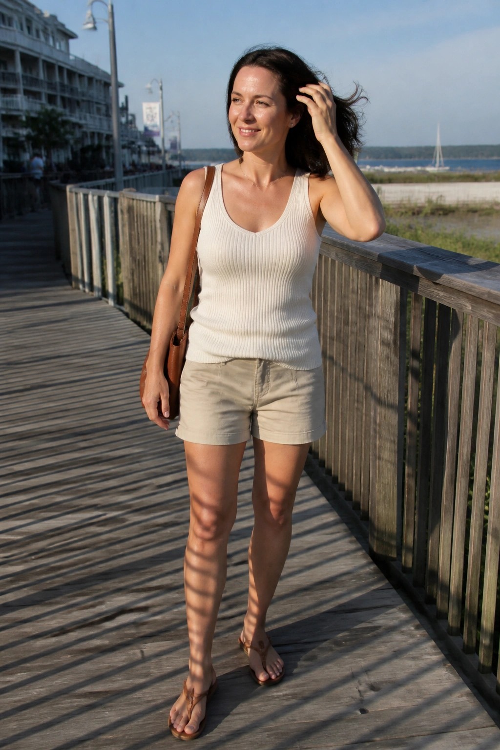 Woman in white tank top and khaki shorts on sunny wooden boardwalk by water