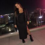 Woman in black satin dress and leather jacket on NYC rooftop at night with I Love NY sign
